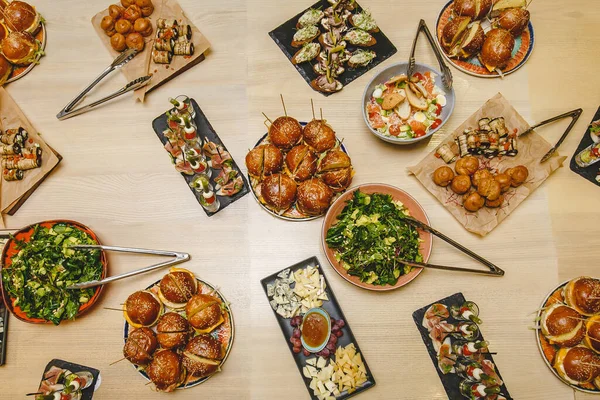 Lokantadaki modern lezzetli yiyeceklerle dolu bir masa. Hamburgerler, atıştırmalıklar, mezeler, salatalar ve peynirler.