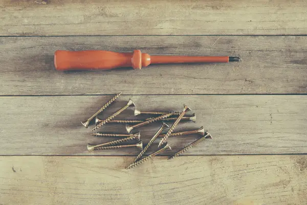 Destornillador y muchos tornillos en un pedazo de madera — Foto de Stock