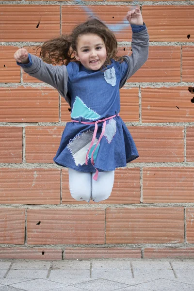 Cheerful girl jumping against of brick wall — Stock Photo, Image