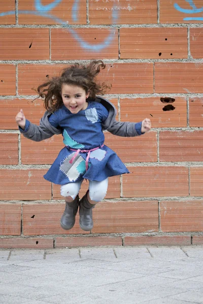 Glad flicka hoppar mot av tegelvägg — Stockfoto