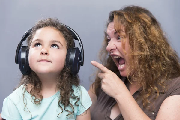 Piękne dziewczyny w słuchawki patrząc w górę podczas gdy jej matka krzyczy z palcem wskazującym — Zdjęcie stockowe
