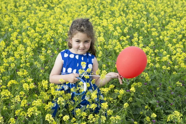 Sorridente ragazza bruna che gioca con palloncino rosso in campo giallo brillante — Foto Stock