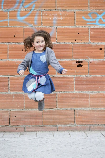 Cheerful girl jumping against of brick wall — Stock Photo, Image