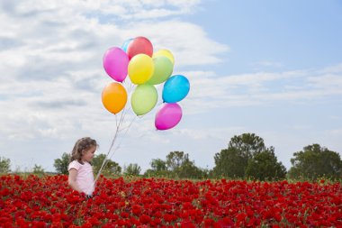 Kır çiçekleri ve birçok renkli balonlar alanında küçük kız