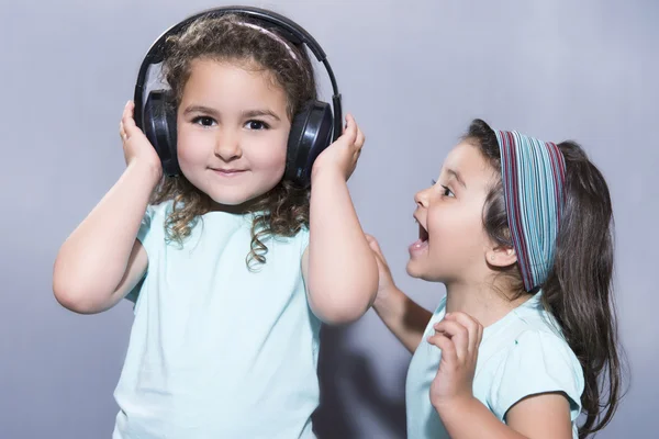 Sonriente chica escuchando música en los auriculares con la hermana gritando cerca —  Fotos de Stock