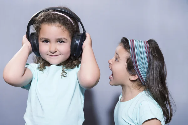 Smiling girl listening to music in headphones with sister scream — Stock Photo, Image