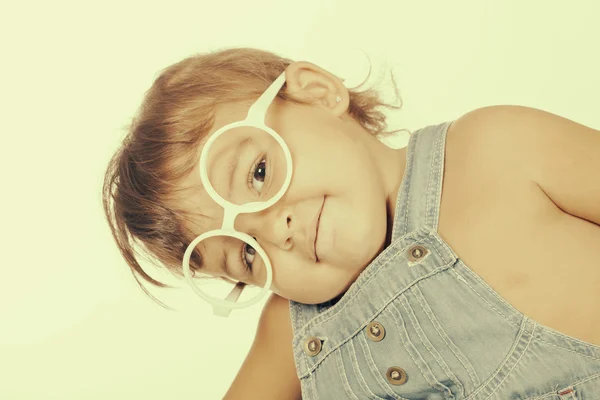Little girl wearing overall and white glasses looking at camera — Stock Photo, Image