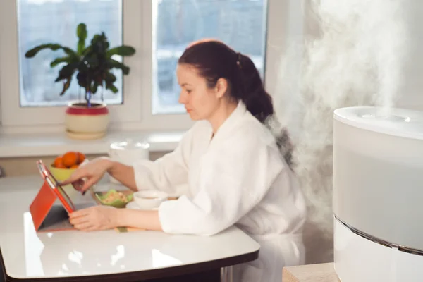 Woman sitting with tablet PC on the background of humidifier — Stock Photo, Image