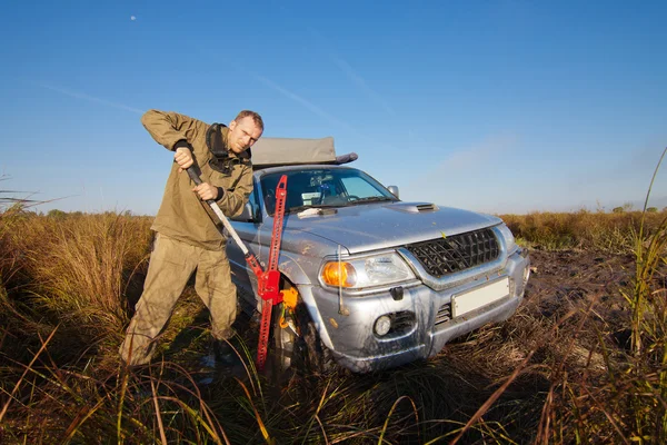 Mann hebt Auto mit Wagenheber in tiefen Schlamm — Stockfoto