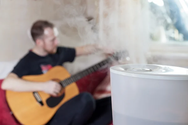 Man tuning his guitar on the background of humidifier — Stock Photo, Image