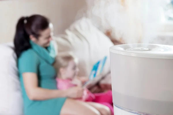 Mamma läsa boken till sin dotter på bakgrund av humidif — Stockfoto