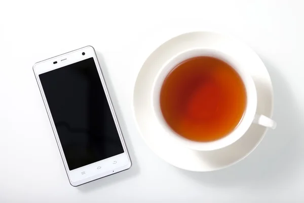 Smartphone branco e uma xícara de chá na mesa de vidro branco Imagem De Stock