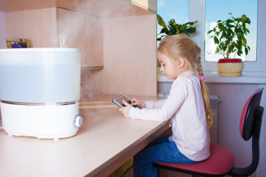 Little girl with tablet pc sitting near humidifier clipart