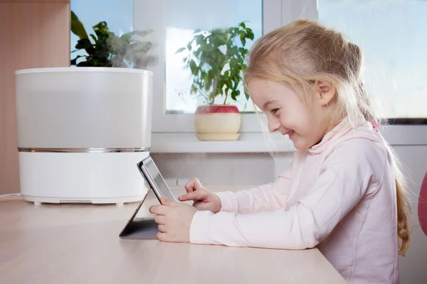 Little girl with tablet pc sitting near humidifier and smiling — Stock Photo, Image