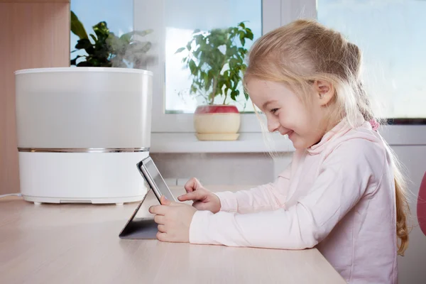 Niña con tableta pc sentado cerca del humidificador y sonriendo —  Fotos de Stock