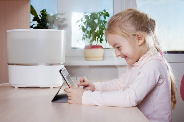 Little girl with tablet pc sitting near humidifier and smiling
