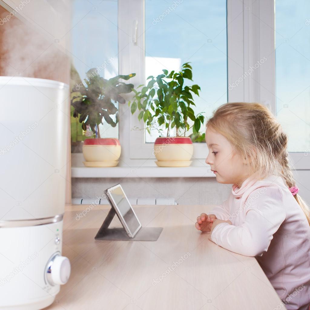 Little girl with tablet pc sitting near humidifier