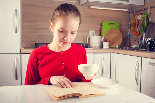 Adolescente chica leyendo libro con una taza de té —  Fotos de Stock