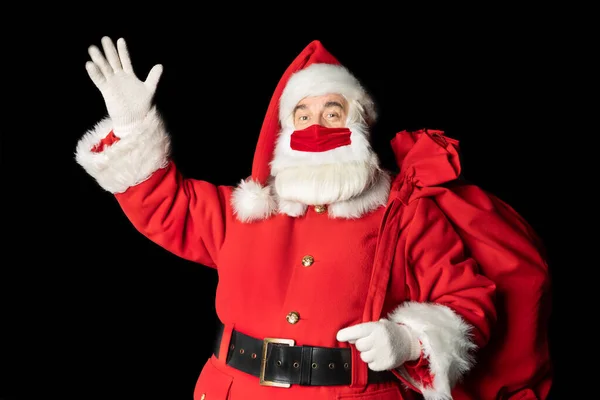 Güzel maskeli Noel Baba elini kaldırarak selamlıyor. Siyah arkaplan.