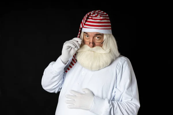 Gecelik giymiş sakallı bir Noel Baba gözlüğünü tutarken aksanlı bakar. Siyah bir arkaplanda.