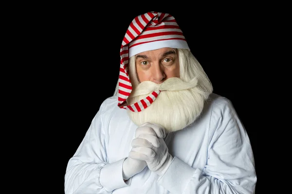 Noel Baba, küçük bir çocuk gibi geceliğiyle yatmadan önce başlığının ucunu ağzına sokuyor. Siyah bir arkaplanda.