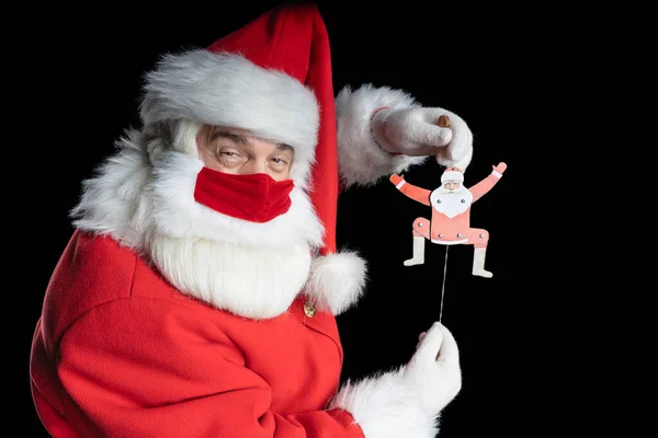 Noel Baba kostümü ve maskeli bir adam, kurnaz gözlü, siyah arka planda Noel Baba 'nın elinde kukla resmi var..