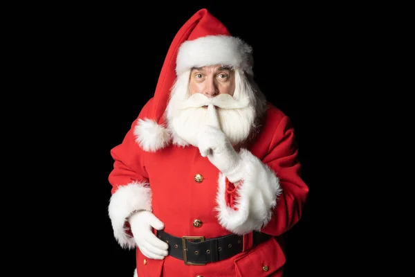 Geleneksel Noel Baba kostümü giymiş sakallı ve gri saçlı yaşlı bir adam parmağını dudaklarına dayayıp sessiz olmak istiyor. Gizli konsept.