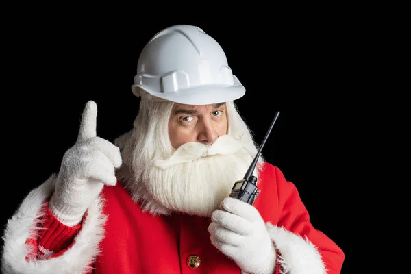 İnşaat kaskındaki Noel Baba telsizle konuşuyor ve izole edilmiş siyah arka plan, Noel endüstrisi kavramına işaret ediyor..
