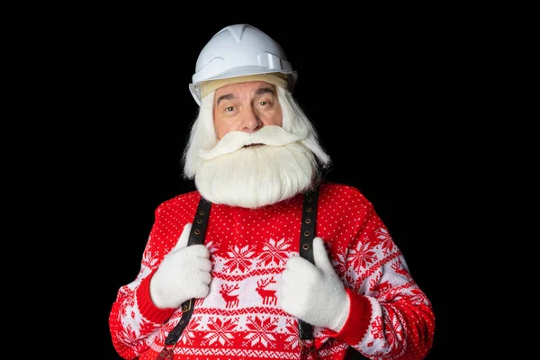 Gri saçlı, Noel Baba süveteri giyen ve kafasında kask olan bir adam ellerini askıların üzerinde tutuyor. Endüstriyel Noel konsepti.