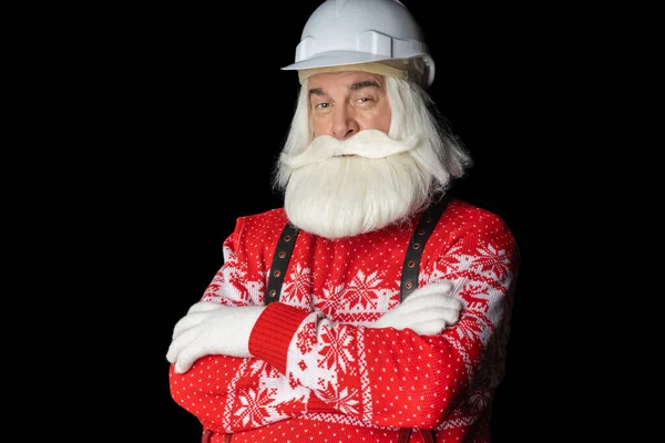 Gri sakallı ve kasklı, elleri katlanmış, Noel Baba süveteri giyen gri saçlı bir adam sinsi görünüyor. Noel Baba Noel Arifesi İnşaat Konsepti.