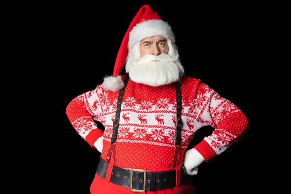 Çatık kaşlı Noel Baba 'nın kıdemli adamı. Stüdyoda siyah arka plana karşı poz verirken ellerinin kalçasında duruyor. Kopya uzayı. İzole edilmiş siyah arkaplan.