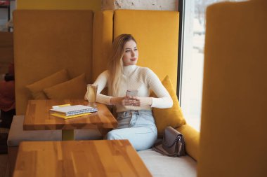 Kafede oturup ders çalışan uzun saçlı güzel sarışın bir kızın portresi.