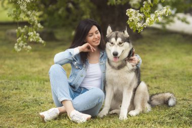 Güzel esmer kız çimlerin üzerinde komik arkadaşı hastalıklı köpekle oturuyor.