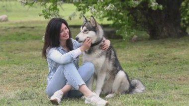 Genç ve güzel bir kadın Alaska 'lı köpekle çimlerin üzerinde oynuyor.