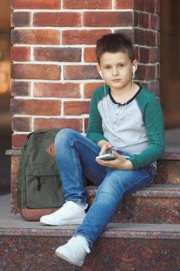 Okul çocuğu okuldan sonra telefonla müzik dinler ya da online oyunlar oynar.