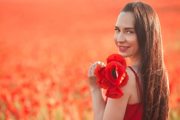 Young brunette woman 25-30 years old with long groomed hair in red dress enjoy a poppy flowers in field — Foto Stock