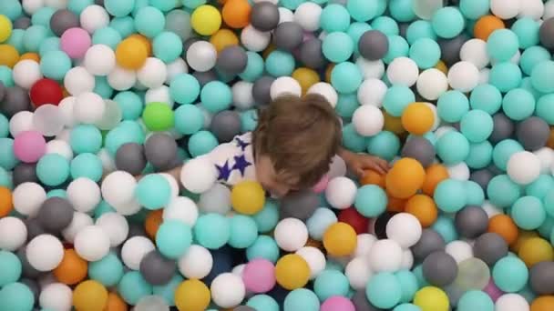 Boldog játékkal teli kisfiú 2-3 éves száraz medencében színes műanyag golyókkal — Stock videók