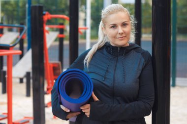 Genç şişman kadın spor yaptıktan sonra sokak idmanında su içiyor. Spor giyim bölümündeki yorgun sarışın kız dışarıda antrenman yaparak kilo vermeye çalışıyor. Yüksek kalite fotoğraf