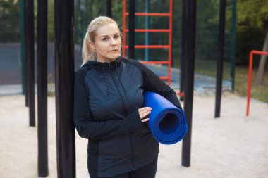 Genç şişman kadın spor yaptıktan sonra sokak idmanında su içiyor. Spor giyim bölümündeki yorgun sarışın kız dışarıda antrenman yaparak kilo vermeye çalışıyor. Yüksek kalite fotoğraf