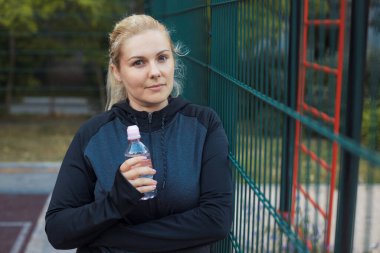 Genç şişman kadın spor yaptıktan sonra sokak idmanında su içiyor. Spor giyim bölümündeki yorgun sarışın kız dışarıda antrenman yaparak kilo vermeye çalışıyor. Yüksek kalite fotoğraf