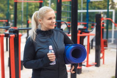 Genç şişman kadın spor yaptıktan sonra sokak idmanında su içiyor. Spor giyim bölümündeki yorgun sarışın kız dışarıda antrenman yaparak kilo vermeye çalışıyor. Yüksek kalite fotoğraf