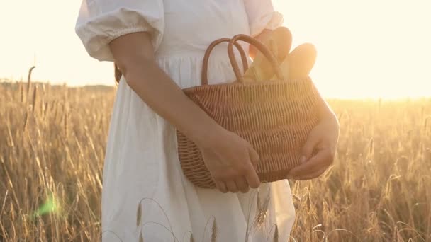 Jovem segurando uma cesta de palha de vime com baguete francesa em um campo de trigo — Vídeo de Stock