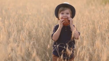 Tatlı ve komik küçük çocuk yaz günü buğday tarlasında taze çörek yiyor. 
