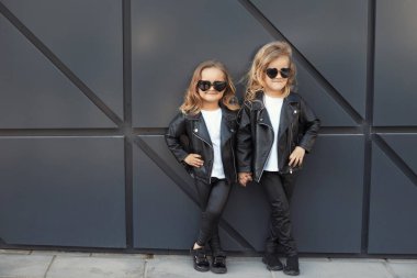Aynı kıyafetleri giyen iki kız kardeş: beyaz tişörtler, siyah deri ceketler ve tozluklar, güneş gözlüğü kalpleri..