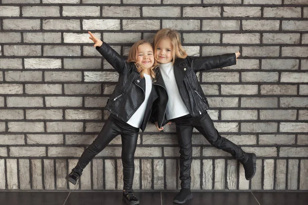 Dos hermanas graciosas con los mismos trajes: camisetas blancas, chaquetas negras de cuero y leggings Fotos de stock libres de derechos