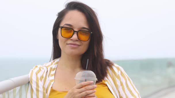 Sorrindo mulher com sobrepeso em óculos de sol amarelos bebe coquetel suculento no dia de verão — Vídeo de Stock