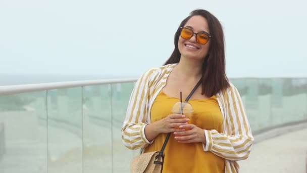 Χαμογελώντας υπέρβαρη γυναίκα σε κίτρινα γυαλιά ηλίου πίνει ζουμερό coctail το καλοκαίρι ημέρα — Αρχείο Βίντεο