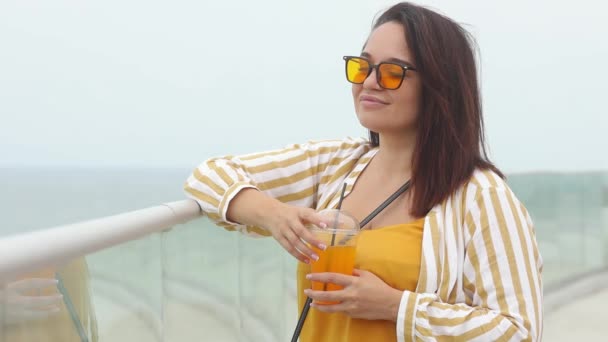 Sorrindo mulher com sobrepeso em óculos de sol amarelos bebe coquetel suculento no dia de verão — Vídeo de Stock