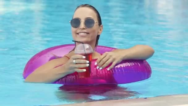 Hermosa chica sonriente en el anillo de natación en la piscina beber cóctel de cereza — Vídeos de Stock