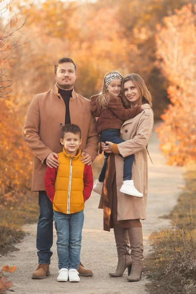 Famiglia felice che si abbraccia in una passeggiata nel parco autunnale. Ritratto di una madre e di un padre caucasici che tengono i loro figli in abiti bellissimi in una soleggiata giornata autunnale nella foresta. Stile di vita familiare concetto. — Foto Stock